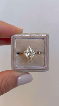 a woman's hand holding an engagement ring in a velvet box with a diamond on it