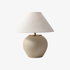 a white table lamp with a beige shade on the base and a light bulb attached to it