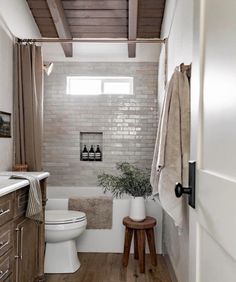 a white toilet sitting next to a bath tub in a bathroom on top of a wooden floor