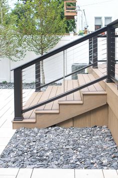 a wooden deck with metal handrails and gravel on the ground next to it