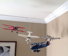 two toy airplanes suspended from the ceiling in a room with a framed photo on the wall