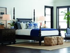 a bedroom with a four post bed, blue and white sheets, pillows, and throw pillows