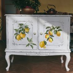 a white cabinet with lemons painted on the doors and drawers is shown in front of a potted plant