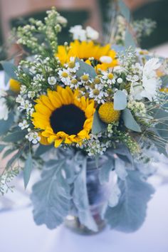 a bouquet of sunflowers and other flowers in a glass vase on a table