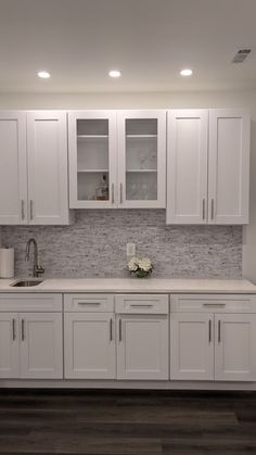 a kitchen with white cabinets and wood flooring is pictured in this image, there are flowers on the counter