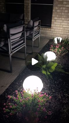 some lights that are sitting in the grass near flowers and chairs on a sidewalk at night