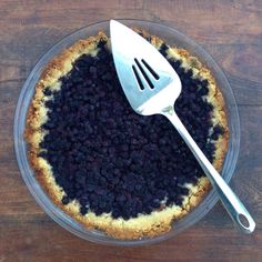 a blueberry pie with a fork in it on a wooden table next to a knife