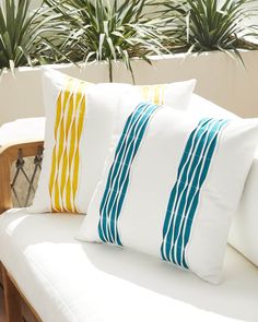 three pillows sitting on top of a white couch in front of some plants and potted plants