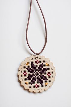 a cross stitch ornament hanging from a cord on a white surface with a black and red bead design