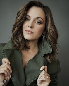 a woman in a green jacket is posing for a photo with her hands on her chest