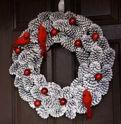 a pine cone wreath with red balls and cardinal cardinals on the front door for christmas