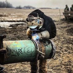 a man with goggles and a gas mask is carrying a barrel in the mud