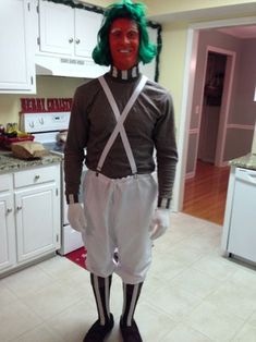 a man with green hair and suspenders standing in a kitchen next to white cabinets