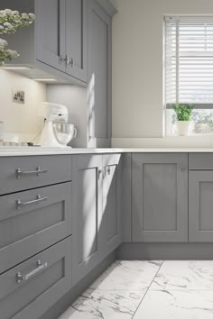 a kitchen with gray cabinets and white counter tops is pictured in this image, there are flowers on the window sill