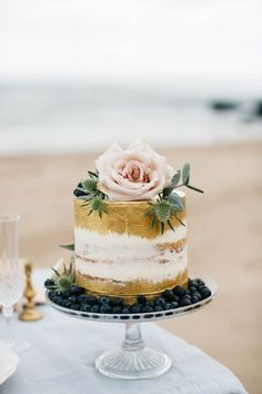 the cake is decorated with flowers and greenery on the table next to the ocean