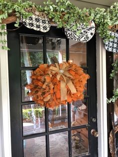 a wreath on the front door of a house with pumpkins and greenery around it