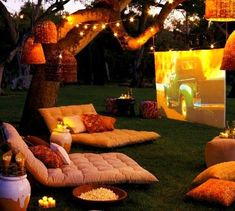 an outdoor movie is set up in the grass with lights strung over it and pillows on the ground