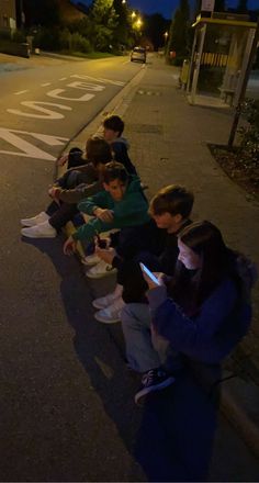 several people sitting on the curb with their cell phones in their hands and looking at them