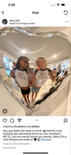 two people standing in front of a heart shaped mirror with the reflection of them on it