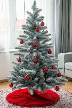 a white christmas tree with red ornaments on it in front of a window and rug