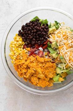 a bowl filled with black beans, corn, lettuce, cheese and other toppings