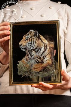 a woman holding up a painting of a tiger