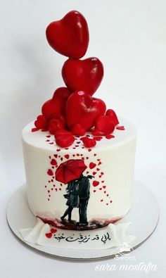 a white cake with red hearts on top and a couple holding an umbrella in the middle