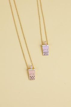 two gold necklaces with pink and white designs on them, one has a small square pendant