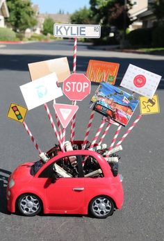 a small red car with lots of stickers on it's hood parked in front of a street sign