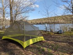 a tent is pitched up on the ground next to a lake and trees with no leaves