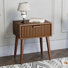 a nightstand with books on it and a lamp next to it in front of a white wall