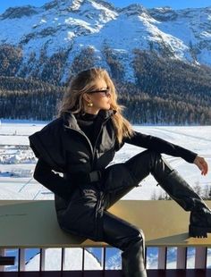 a woman sitting on top of a wooden bench in front of snow covered mountain range