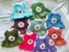 several crocheted hats are arranged on a white sheet with daisies in the center