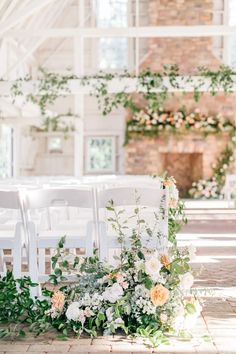 an outdoor ceremony setup with white chairs and greenery on the aisle, along with floral arrangements