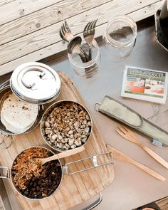 a wooden tray topped with lots of food next to utensils and spoons