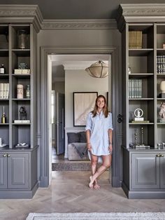 a woman standing in the doorway of a room with gray bookcases and shelving