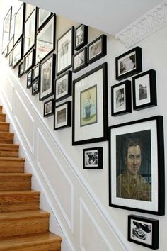 there are many framed pictures on the wall next to the stair case and handrail