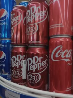 several cans of soda are on display in a grocery store, one is red and the other is blue