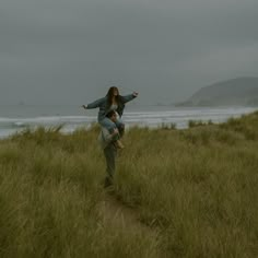 two people standing in tall grass near the ocean