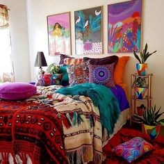 a bed with colorful blankets and pillows in a room filled with paintings on the wall