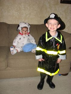 two children dressed in costumes sitting on a couch next to each other and one is wearing a fireman costume