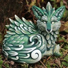 a green and white figurine sitting on the ground next to some grass with leaves