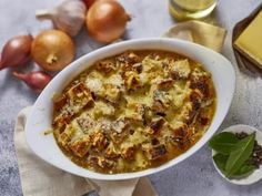 a white bowl filled with food on top of a table next to onions and cheese