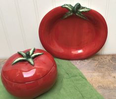 two red ceramic tomatoes sitting on top of a green place mat next to each other