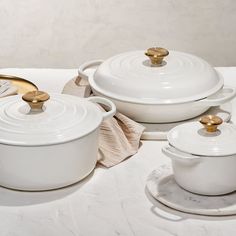 a table topped with white pots and pans covered in gold rimmed dishes next to glasses