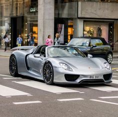 a silver sports car is driving down the street in front of some people and cars