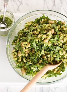 a glass bowl filled with pasta and greens next to a measuring cup full of pesto