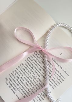 an open book with a pink ribbon tied around it and some pearls on the pages