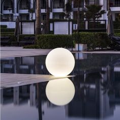 a white ball sitting on top of a pool next to tall buildings and palm trees