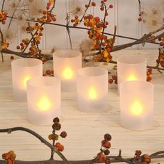 four white candles sitting on top of a wooden table next to branches with flowers and berries